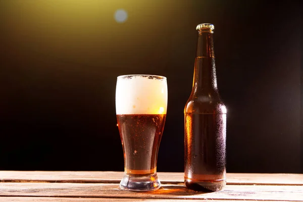 Kaltes, schmackhaftes Bier an heißen Sommertagen. Flasche und Glas Bier auf einem Holztisch vor schwarzem Hintergrund und Kopierraum — Stockfoto