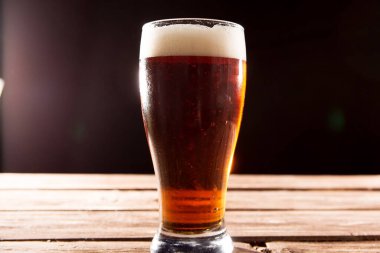 Sıcak yaz gününde soğuk, lezzetli bira. Siyah arka plandaki ahşap masada bir bardak bira.