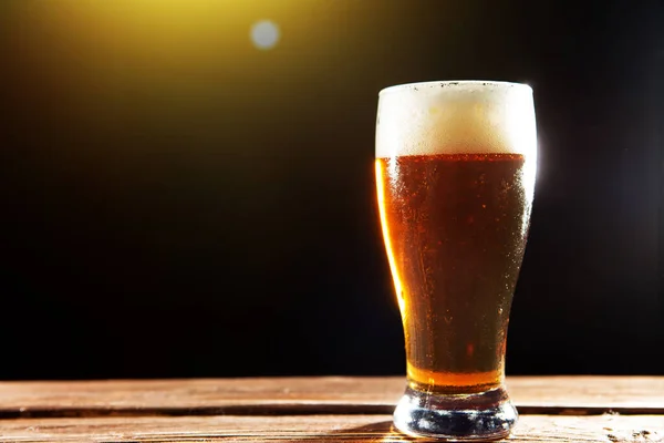 Birra fresca e gustosa nella calda giornata estiva. Bicchiere di birra su tavolo di legno su sfondo nero — Foto Stock