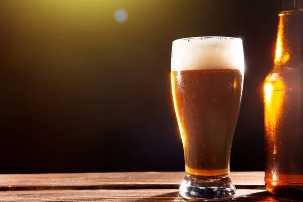 Zimne, smaczne piwo w upalny letni dzień. Butelka i szklanka piwa na drewnianym stole na czarnym tle i przestrzeni do kopiowania — Zdjęcie stockowe