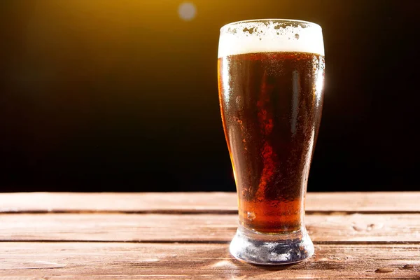 Bière fraîche et savoureuse pendant la chaude journée d'été. Verre de bière sur table en bois sur fond noir — Photo