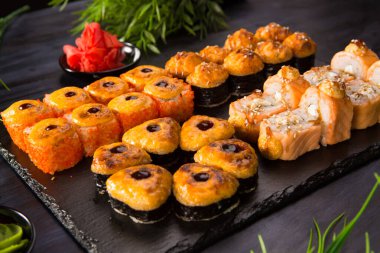 Siyah arka planda wasabi ve zencefilli fırında suşi ruloları. Japon Doğu mutfağı.
