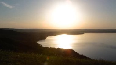 Bir dağ gölünün arka planındaki kız, deniz ya da okyanus ellerini yukarı kaldırır ve gün batımında özgürlüğün tadını çıkarır.