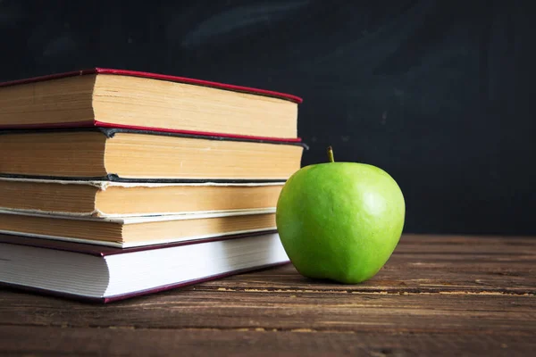 Boeken en appels op houten tafel tegen de achtergrond van het schoolbord of schoolbord. — Stockfoto