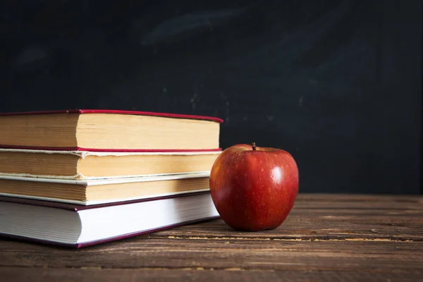 Boeken en appels op houten tafel tegen de achtergrond van het schoolbord of schoolbord. — Stockfoto