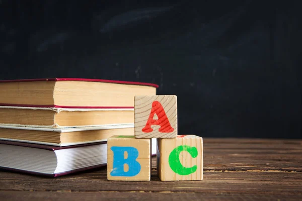 Libri e cubi con le lettere ABC sul tavolo in legno sullo sfondo della lavagna. — Foto Stock