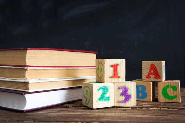 Libri, mele e cubi con le lettere ABC sul tavolo di legno sullo sfondo della lavagna. — Foto Stock