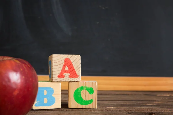 Apple and cubes with the letters ABC on wooden table against the background of the chalkboard. — Stock Photo, Image