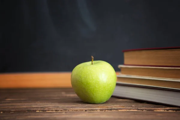 Books and apples on wooden table against the background of the chalkboard or blackboard. — Stock Photo, Image