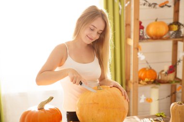 Cadılar Bayramı istilasına hazırız. Gülümseyen genç kadın Cadılar Bayramı süslemeli mutfakta kurabiye ve balkabağı örtüyor..