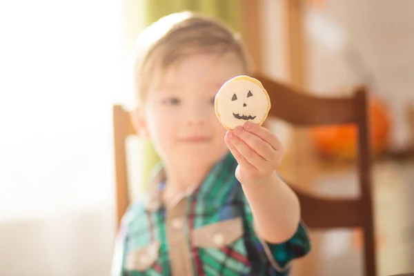 Feliz conceito de Halloween. Bonito menino feliz esculpindo uma abóbora e biscoitos decorados para o Halloween na mesa dentro de casa. — Fotografia de Stock