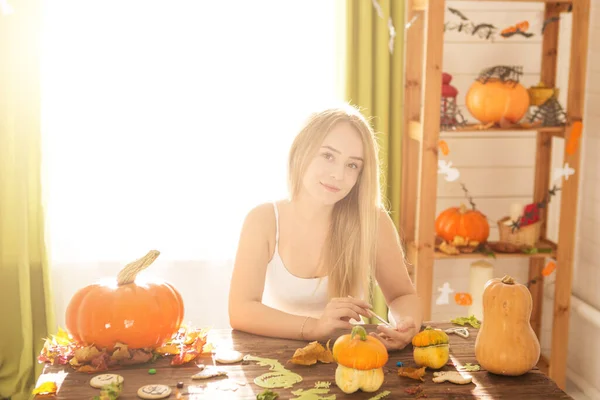 Happy Halloween. Attractive young woman is preparing to Halloween on kitchen. Beautiful woman is painting pumpkins on the background.