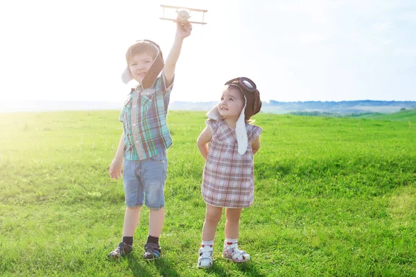 Bruder und Schwester in Pilotenanzügen gehen im Feld spazieren. Reisen schon in der Kindheit. — Stockfoto