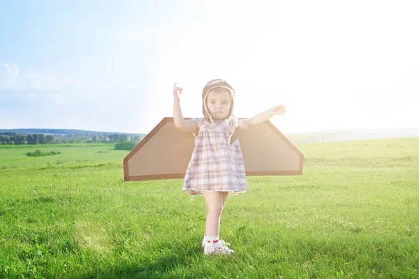 Commencez à voyager dès l'enfance, même dans l'imagination. Enfant fille mignonne rester et jouer dans les pilotes chapeau sur le terrain à l'heure du coucher du soleil avec plaisir — Photo