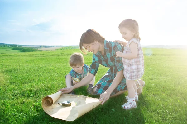 Eine schöne junge Mutter mit ihren Kindern betrachtet eine Weltkarte und entscheidet, wo sie auf Reisen gehen will. — Stockfoto