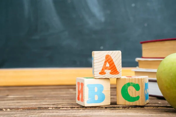 Könyvek és kockák ABC betűkkel a fa asztalon a tábla hátterével szemben. Vissza az iskolába. — Stock Fotó