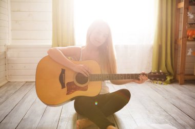 Gitar çalıp şarkı söyleyen bir kız. Uzun saçlı, evde müzik okuyan genç bir kadın. Yerde oturan, akustik gitar çalan ve evde tek başına şarkı söyleyen bir kadın.