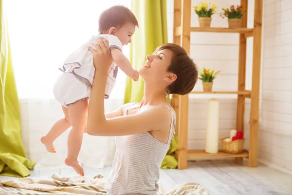 Feliz madre sosteniendo a su hija en alto en sus brazos en una acogedora habitación luminosa —  Fotos de Stock