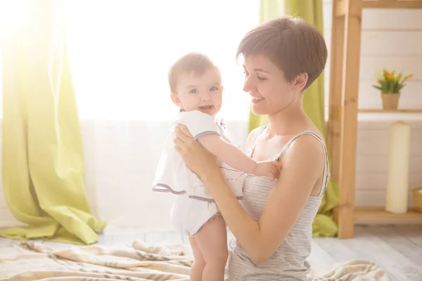 Hermosa mujer y su linda hijita están abrazando y sonriendo mientras están sentados en el suelo en casa —  Fotos de Stock