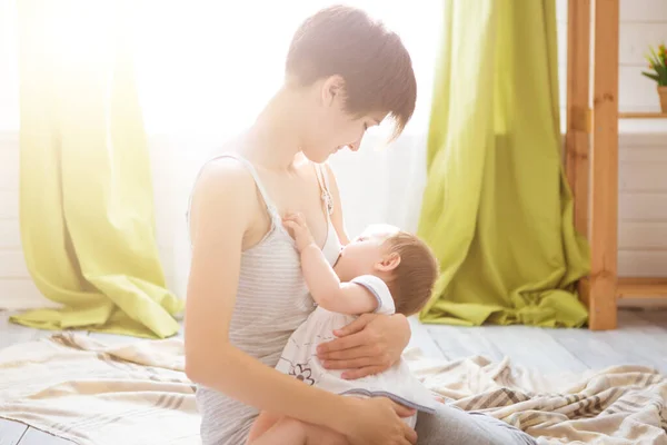 Madre joven sosteniendo a su hijo recién nacido. Mamá amamantando al bebé en un dormitorio blanco. Interior del vivero. Familia en casa —  Fotos de Stock