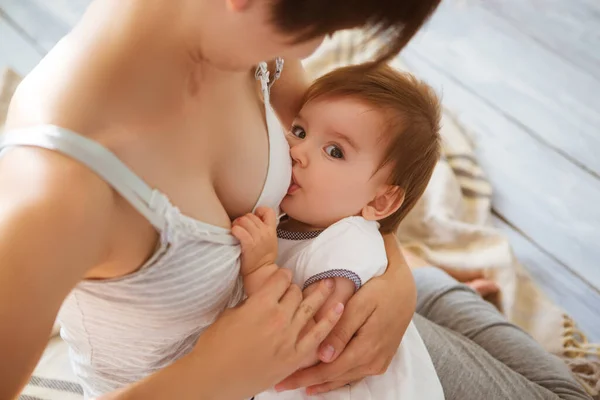 Jovem mãe caucasiana com infante em localização interior. Mãe bebê amamentando em um quarto branco. Interior do berçário. Família em casa — Fotografia de Stock