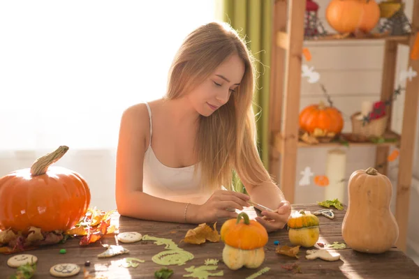 Gotowy do inwazji halloween. Uśmiechnięta młoda kobieta obejmujące ciasteczka i dyni w Halloween urządzone kuchnia — Zdjęcie stockowe