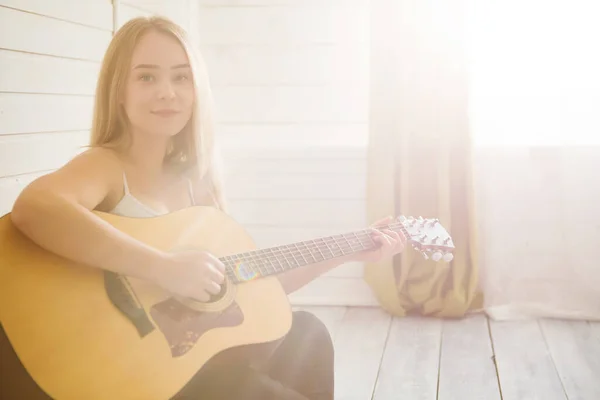 Mujer atractiva con guitarra sentada en sala de luz con suelo de madera. Músico, concierto, hobby, ocio, concepto de ensayo —  Fotos de Stock