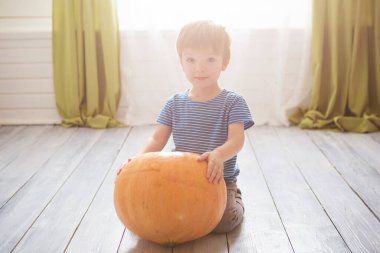 Harika küçük çocuk büyük balkabağıyla oturuyor. Çocuklar küçük çocuğun Cadılar Bayramı 'nı kutlamaya hazır olmasını kutluyorlar. Cadılar bayramı giyinme odasında bir çocuk..