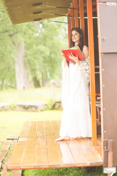 Hübsche Frau im weißen Kleid liest Buch in der bewölkten Natur. Mädchen sitzt auf der Terrasse oder auf der Veranda — Stockfoto