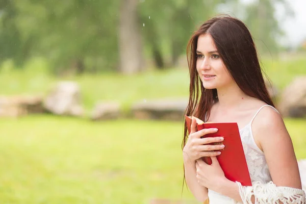 Mujer bonita en vestido blanco libro de lectura en la naturaleza nublada. Chica se sienta en la terraza o en el porche — Foto de Stock