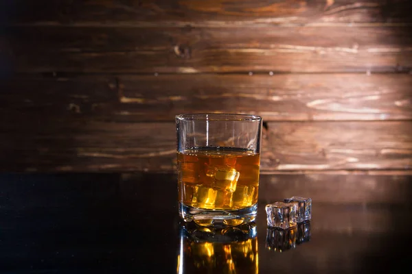 Glas whisky met ijsblokjes op donkere houten ondergrond — Stockfoto