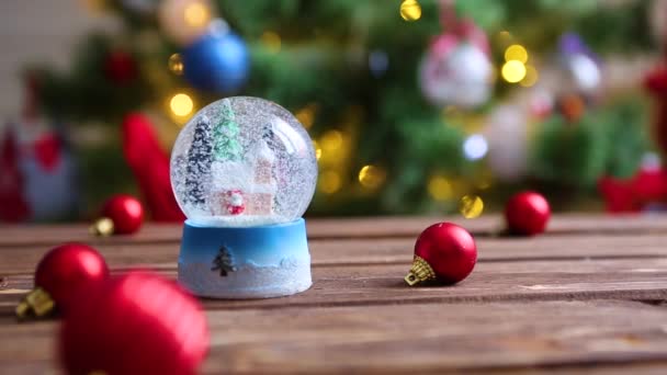 Boule de verre de neige de Noël sur fond d'arbre de Noël avec lumières de Noël — Video