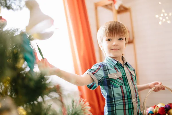 Lindo niño de unos cinco años con ojos azules en un sombrero de Papá Noel decorando un árbol de Navidad —  Fotos de Stock