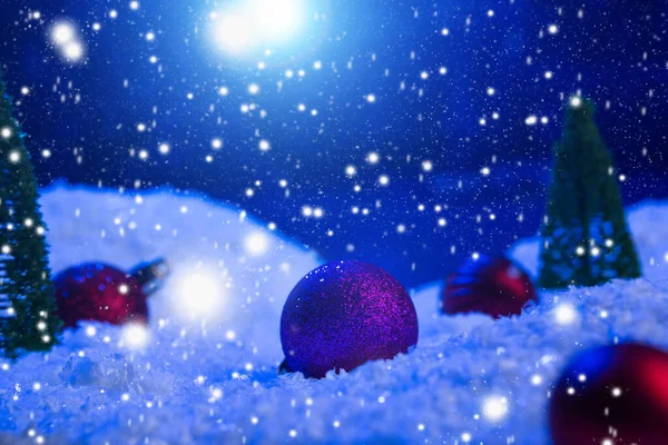 Sfondo natalizio con palline di Natale sulla neve sopra abete, cielo notturno e luna. Profondità di campo ridotta. Sfondo natalizio. Una favola. Macro. Magia artificiale mondo sognante. — Foto Stock