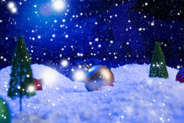Sfondo natalizio con palline di Natale sulla neve sopra abete, cielo notturno e luna. Profondità di campo ridotta. Sfondo natalizio. Una favola. Macro. Magia artificiale mondo sognante. — Foto Stock