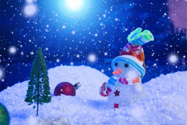 Homem de neve com bolas de Natal na neve sobre abeto, céu noturno e lua. Profundidade de campo rasa. Fundo de Natal. Conto de fadas. Macro. Mundo de sonho mágico artificial. — Fotografia de Stock