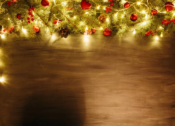 Šedé dřevěné vánoční pozadí s jedlovou větví a červenými vánočními ozdobami v rohu. Rámeček. Pohled shora — Stock fotografie