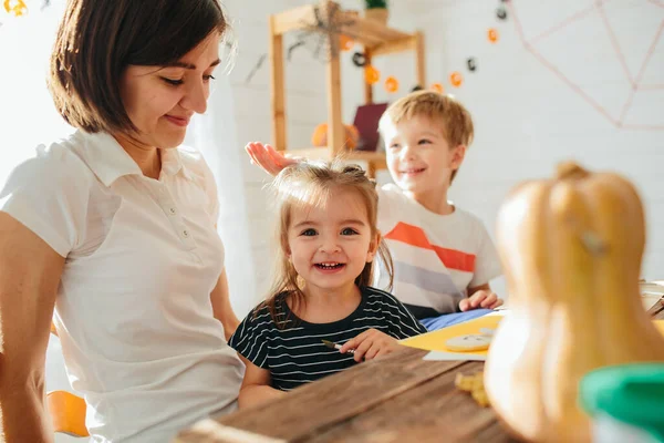 Frohes Halloween. Attraktive junge Frau mit ihren kleinen niedlichen Kindern bereiten sich auf Halloween in der Küche vor und haben Spaß mit Kürbissen. Happy-Halloween-Konzept — Stockfoto