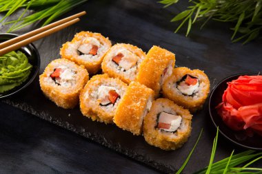 Siyah arka planda wasabi ve zencefilli fırında suşi ruloları. Japon Doğu mutfağı.