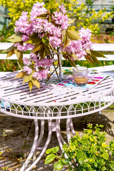 Beautiful and romantic scene in the home garden with a vase of Japanese cherry tree blossoms on the white table