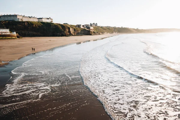 WHITBY in ENGLAND. People walking on Whitby beach on a fine sunny, windy day. In Whitby, North Yorkshire, England.