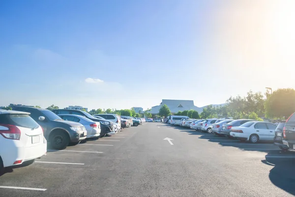 Car parking in large asphalt parking lot with trees, sunlight and blue sky background in front of hall building. Outdoor parking lot with fresh ozone and green environment concept