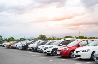 Ağaçlı ve bulutlu arka planlı asfalt otoparkta araba parkı. Açık hava otoparkı, taze ozon ve yeşil ulaşım ortamı ve modern teknoloji konsepti.