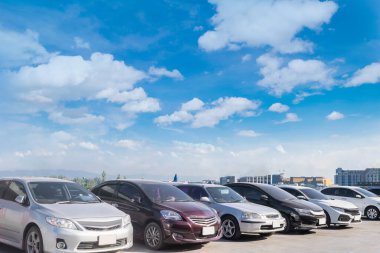 Beyaz bulutlu ve mavi gökyüzü arka planlı büyük bir asfalt otoparkta, koridor binasının önünde. Temiz ozon ve yeşil çevre kavramlı açık hava otoparkı.