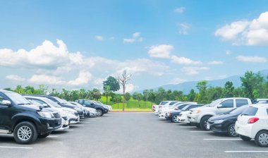 Ağaçlı, beyaz bulutlu, mavi gökyüzü ve dağ zeminli büyük asfalt otoparka park edilmiş bir araba. Taze ozon ve yeşil seyahat taşıma konsepti olan açık hava otoparkı.