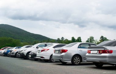 Dağların yanındaki asfalt otoparkta bulutlu gökyüzü manzaralı arabalar.