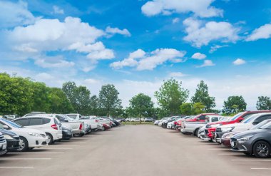 Ağaçlı, beyaz bulutlu, mavi gökyüzü arka planlı büyük bir asfalt otoparka park edilmiş bir araba. Taze ozon ve yeşil seyahat taşıma konsepti olan açık hava otoparkı.