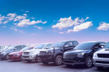 Beyaz bulutlu ve mavi gökyüzü arka planlı asfalt otoparkta araba parkı. Açık hava otoparkı, taze ozon ve yeşil ulaşım konseptiyle.