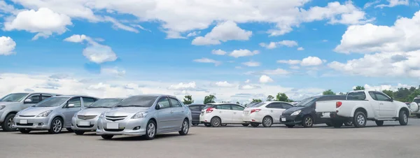 Güneşli bir günde, büyük asfalt otoparkta beyaz bulutlu ve mavi gökyüzü arka planlı bir araba parkı. Açık hava otoparkı, taze ozon ve yeşil ulaşım ve teknoloji konsepti ortamı.