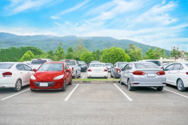 Arabalar asfalt otoparka park edilmiş ve doğada ağaçlar, bulutlar, mavi gökyüzü ve dağ manzaralı boş alan parkı. Temiz ozon ve çevre dostu yeşil çevre kavramına sahip açık hava otoparkı.